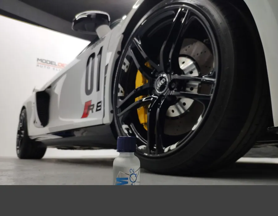 Llanta negra de un Audi R8 con pinza de freno amarilla, junto a un producto de mantenimiento.
