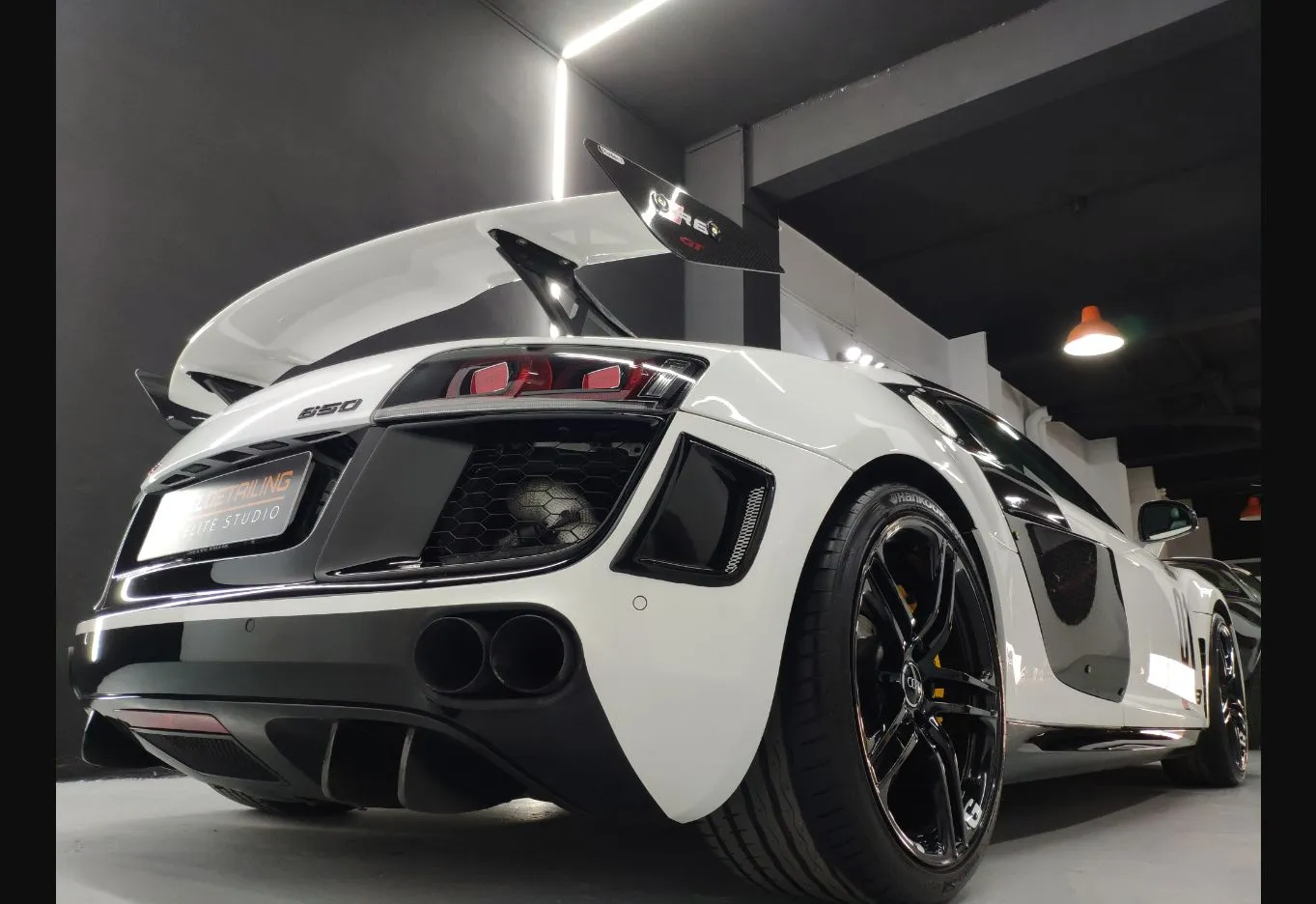 Audi R8 blanco fotografiado desde atrás, con el alerón levantado, mostrando líneas de carrocería y acabados en fibra de carbono.