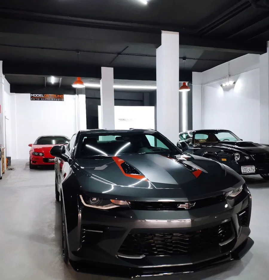 Interior del estudio de Model Detailing con varios vehículos, incluido un Chevrolet Camaro, bajo iluminación de trabajo.