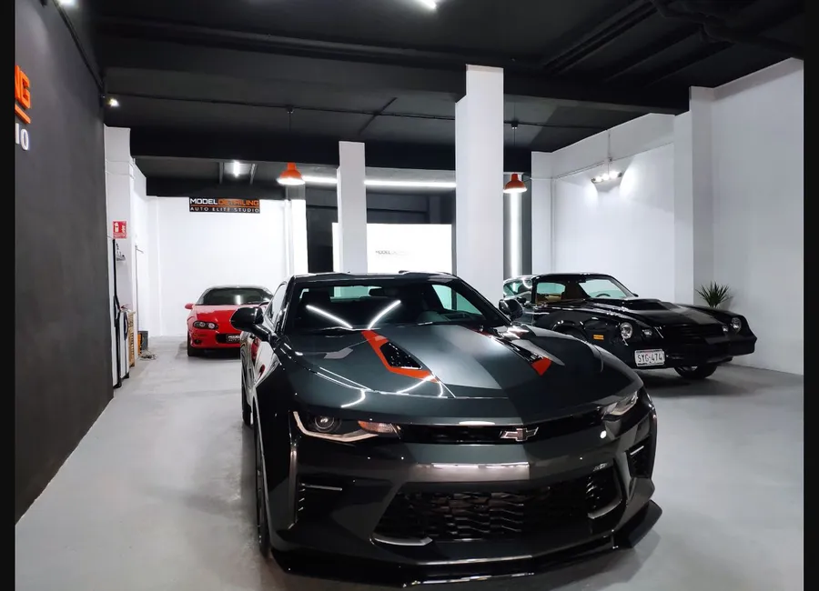 Interior del estudio de Model Detailing con varios vehículos bajo iluminación de trabajo.