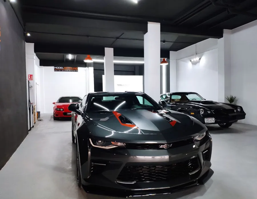 Interior del estudio de Model Detailing con varios vehículos, incluido un Chevrolet Camaro, bajo iluminación de trabajo.