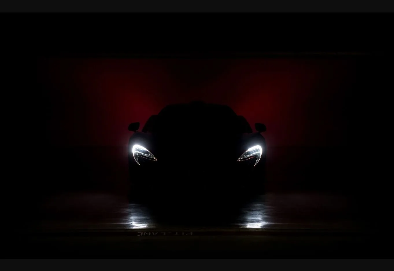 Deportivo fotografiado de frente en penumbra, con los faros encendidos y un fondo rojo intenso, en el estudio de Model Detailing.