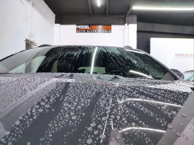 Gotas de agua deslizándose sobre el capó de un vehículo tratado, con el rótulo de Model Detailing al fondo.