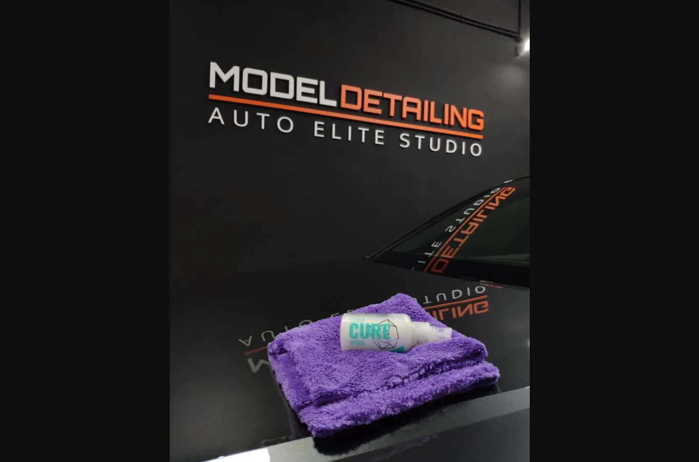 Bote de producto cerámico sobre el capó de un vehículo, con el rótulo de Model Detailing al fondo.